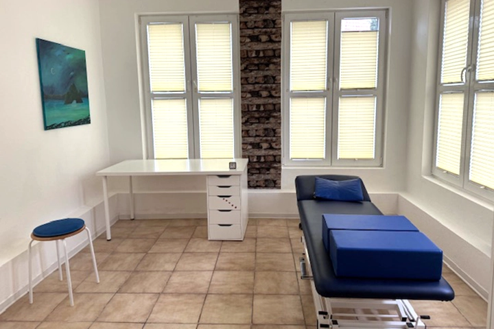 Praxiszimmer mit blauer Liege und weißem Schreibtisch